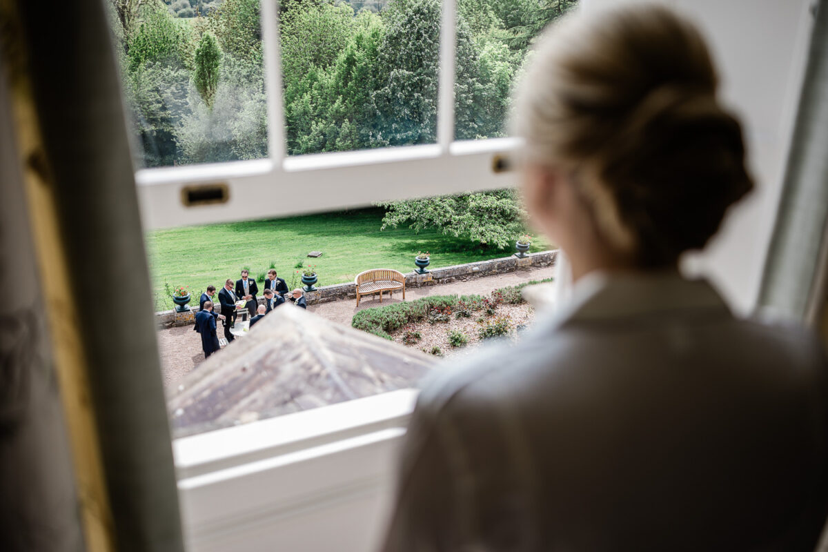 The bride looks out at the groomsmen, before the wedding ceremony at a stately home wedding venue