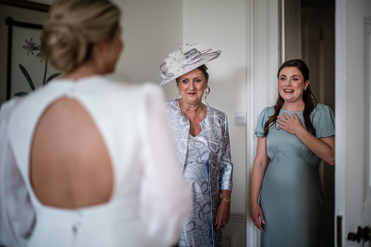 The maid of honour and mother of the bride see the bride for the first time during wedding photography at Pynes House