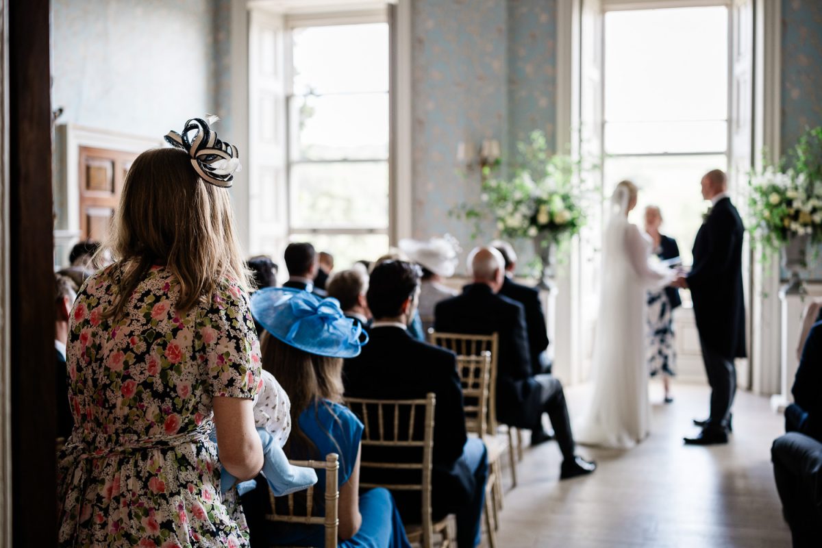 Documentary wedding photographer at Pynes House where a guest watches the bride and groom saying their vows
