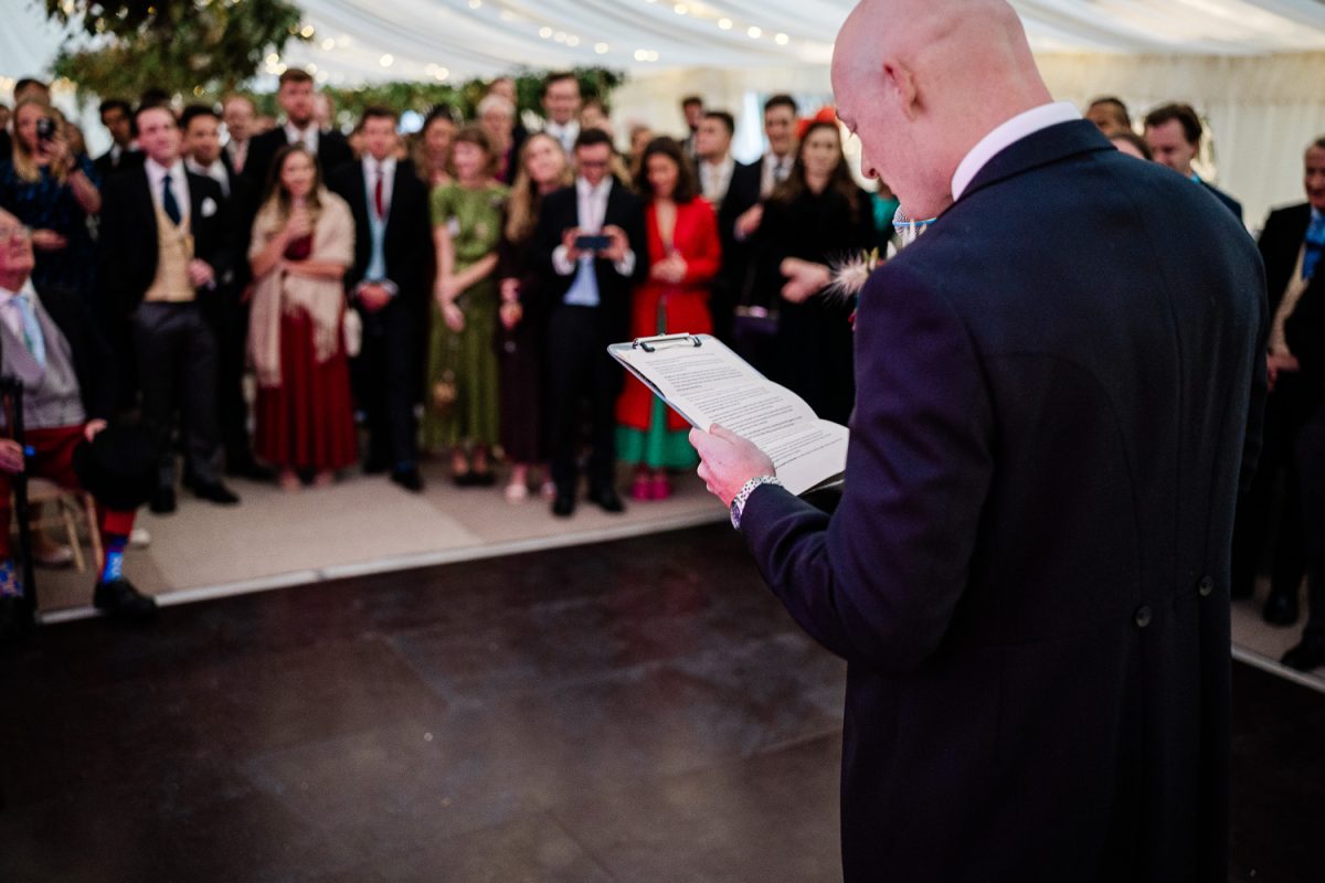 The groom does his wedding speech, as onlooking guests smil